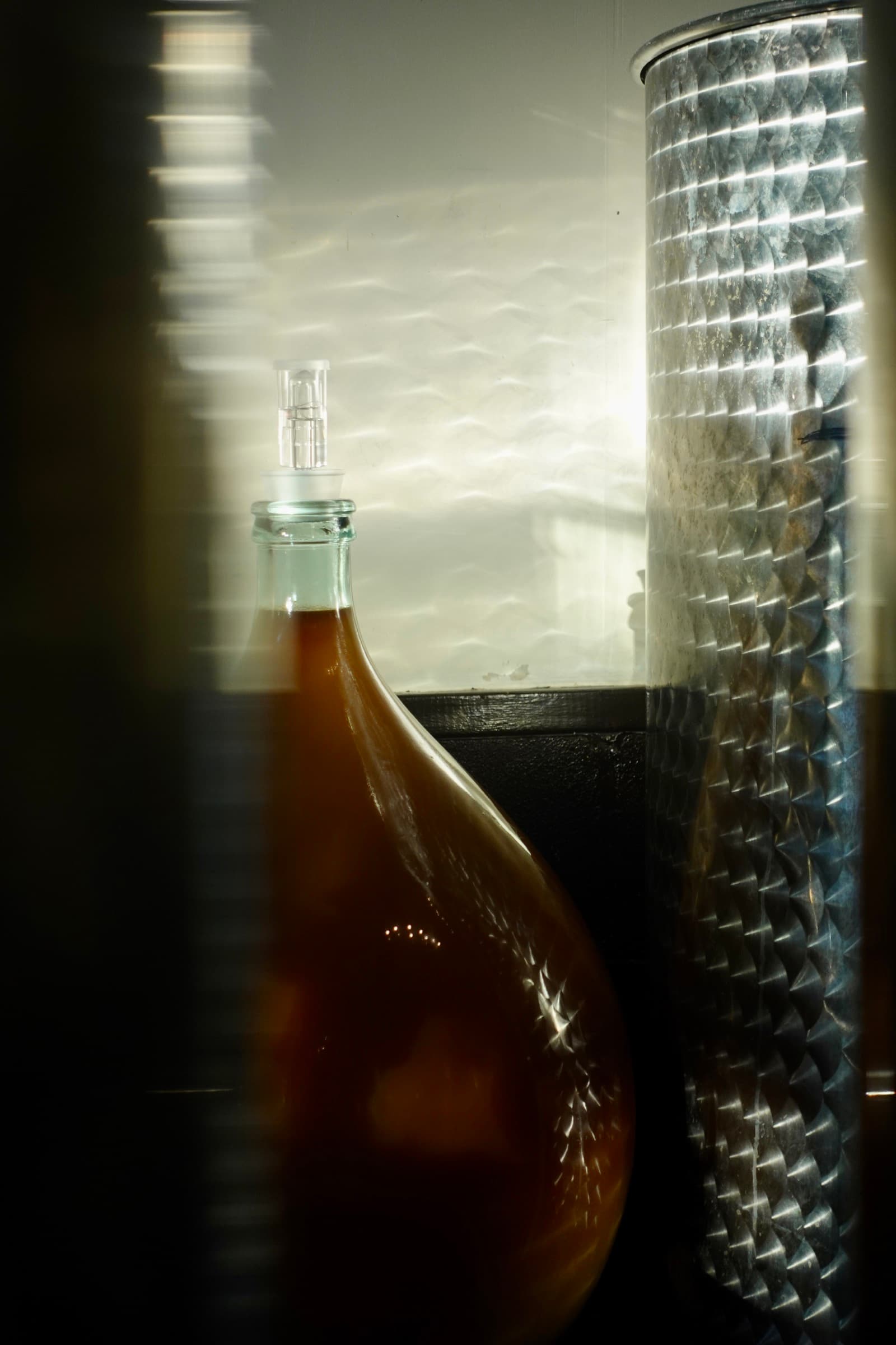 A bottle of cider beside a stainless-steel fermentation tank