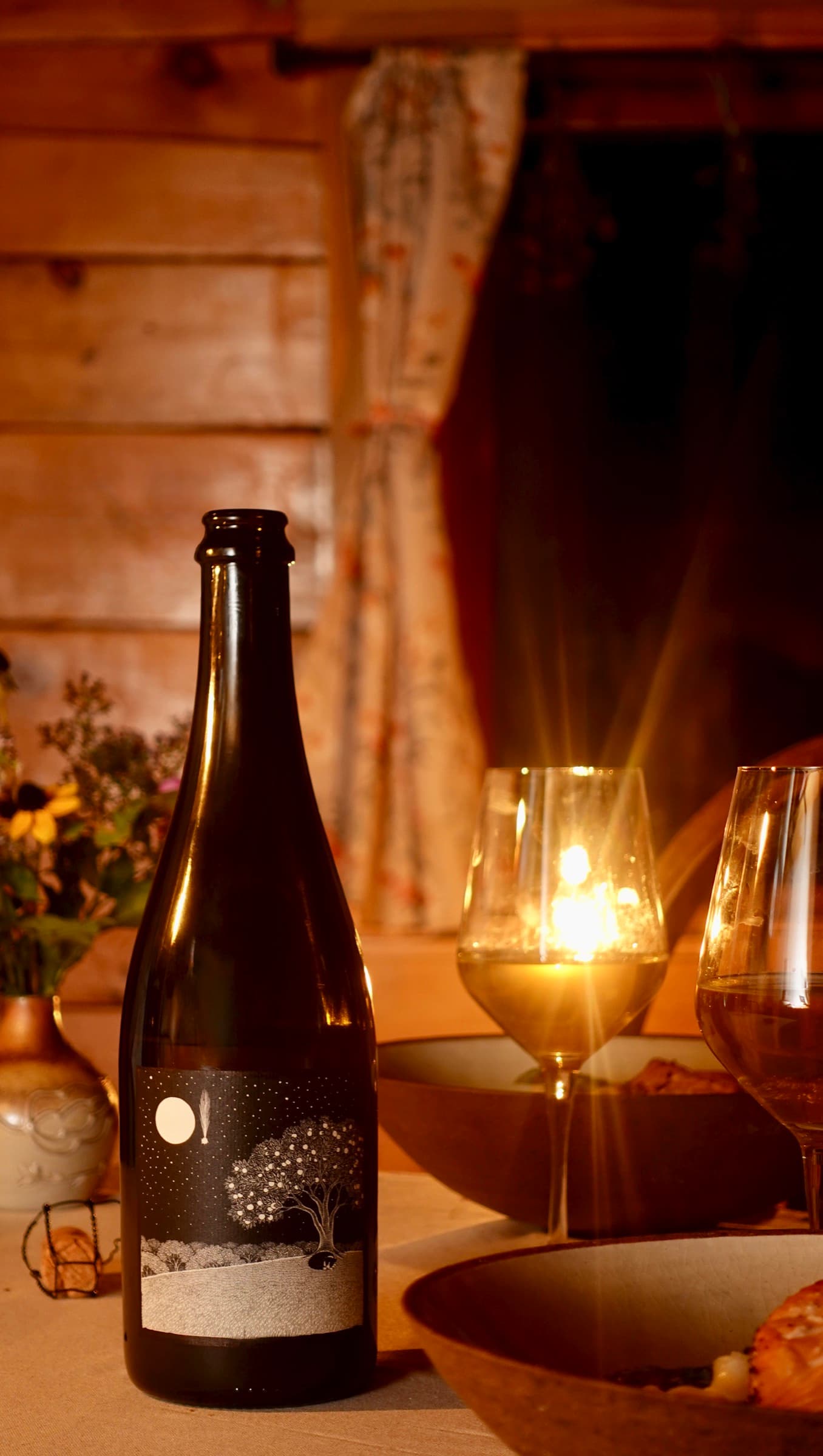 A bottle of cider and glasses on a candlelit table